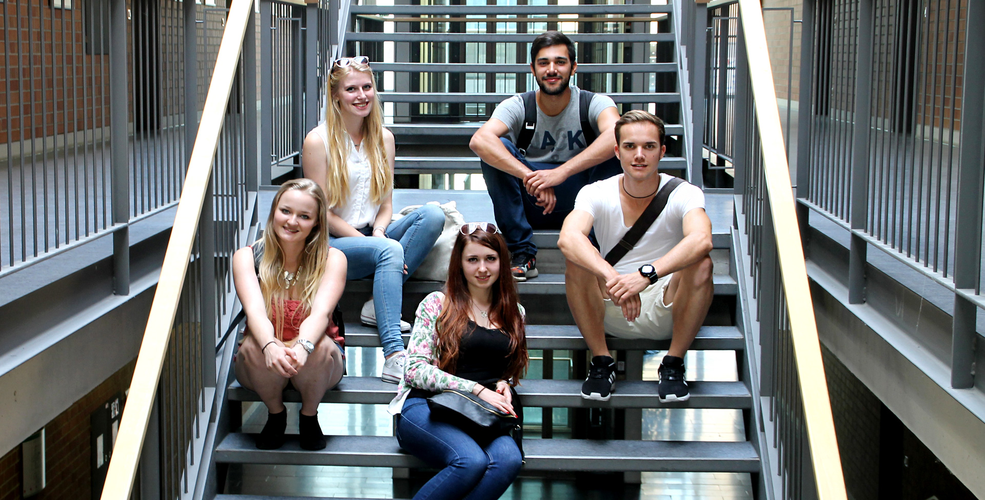 Fünf Studierende sitzen auf einer modernen Treppe, die nach oben führt.